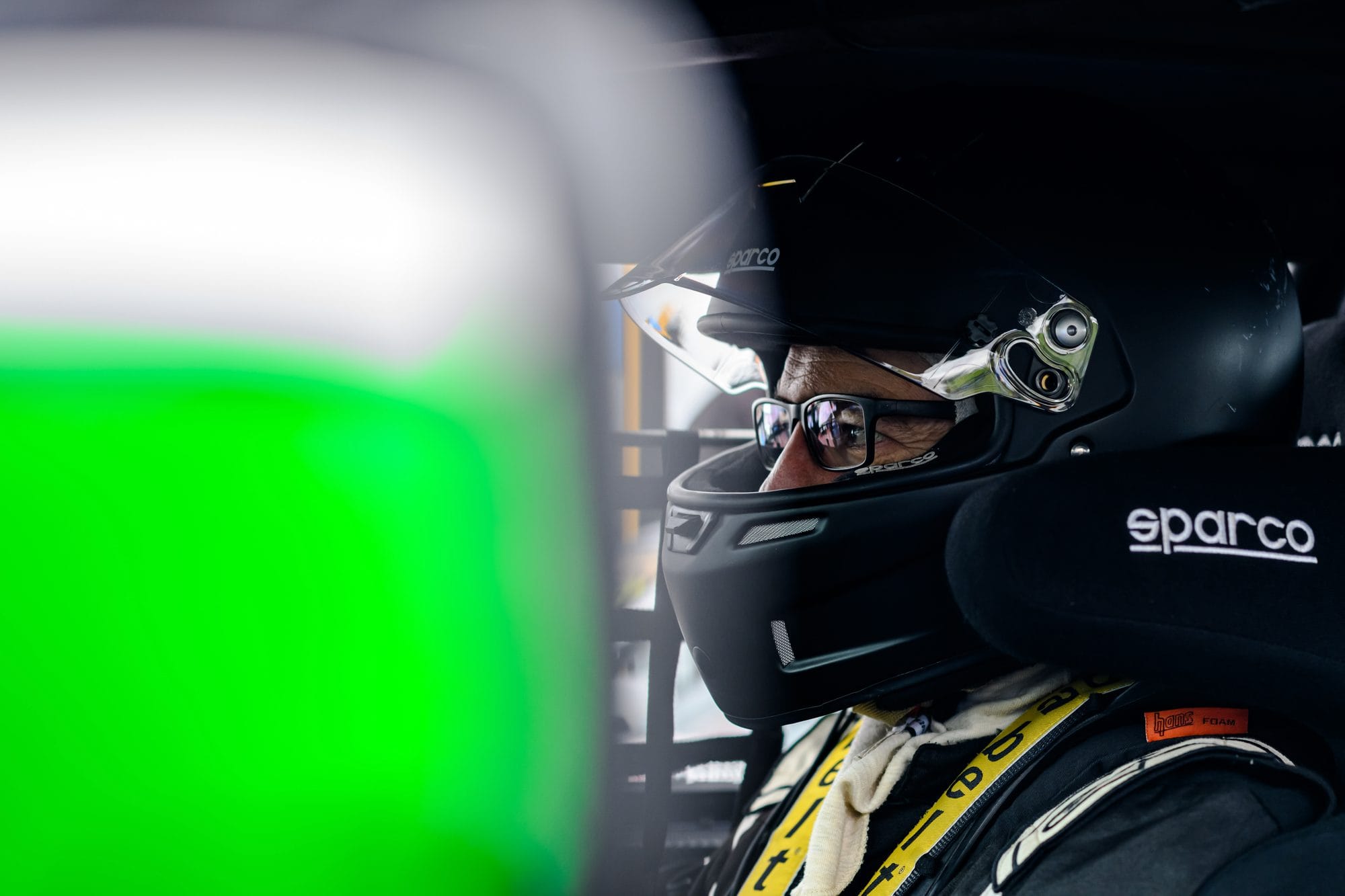 Driver seated in the Project E36 cockpit wearing a black Sparco helmet and HANS device