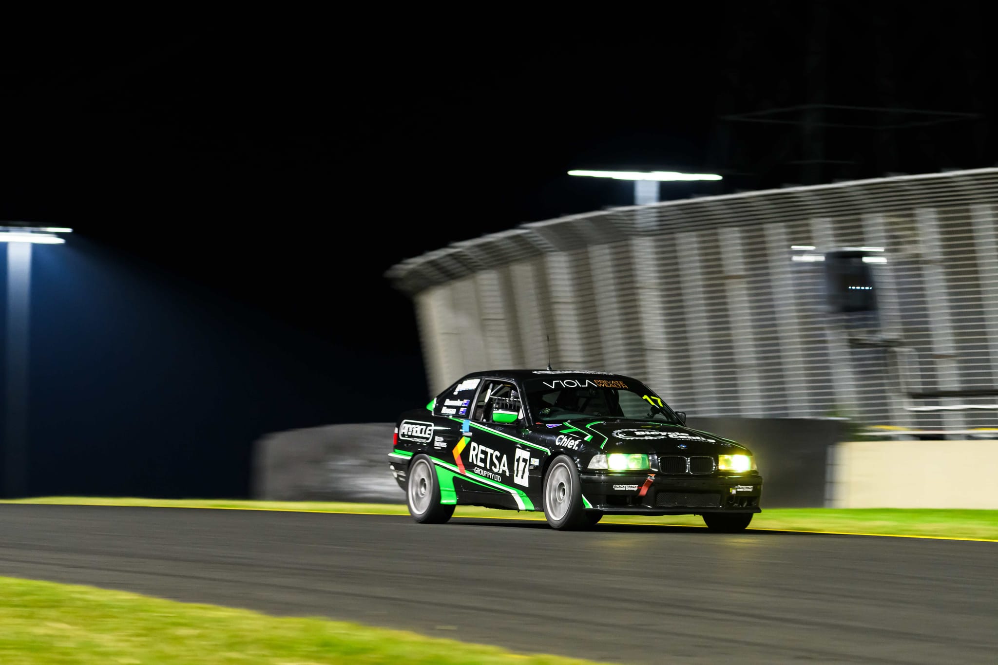 The #17 Project E36 racing under floodlights at night at Sydney Motorsport Park
