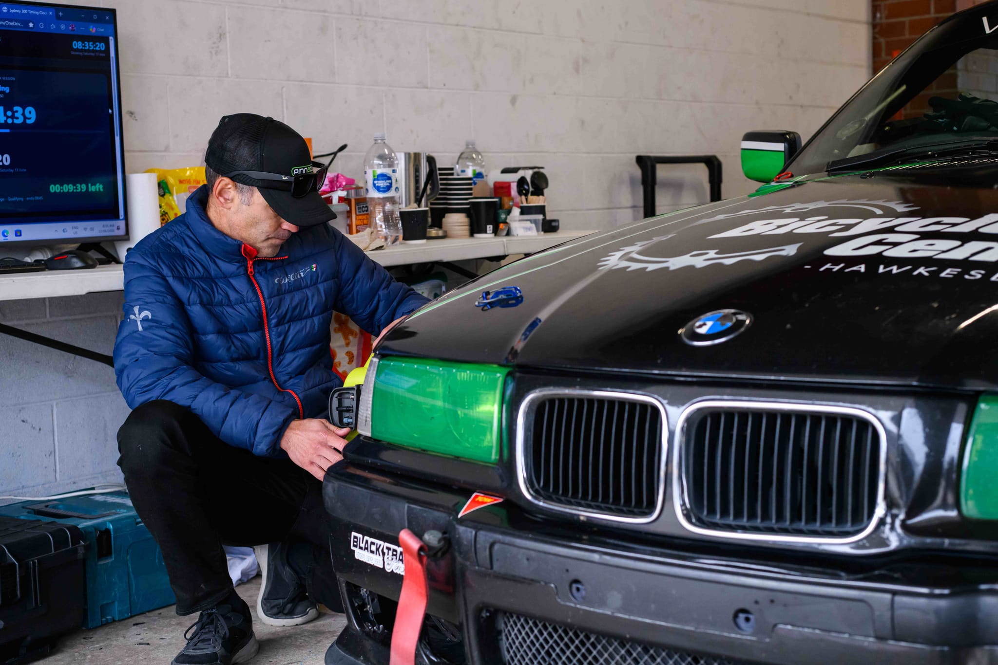 Crew member fitting green headlight covers to the Project E36 in the garage during qualifying