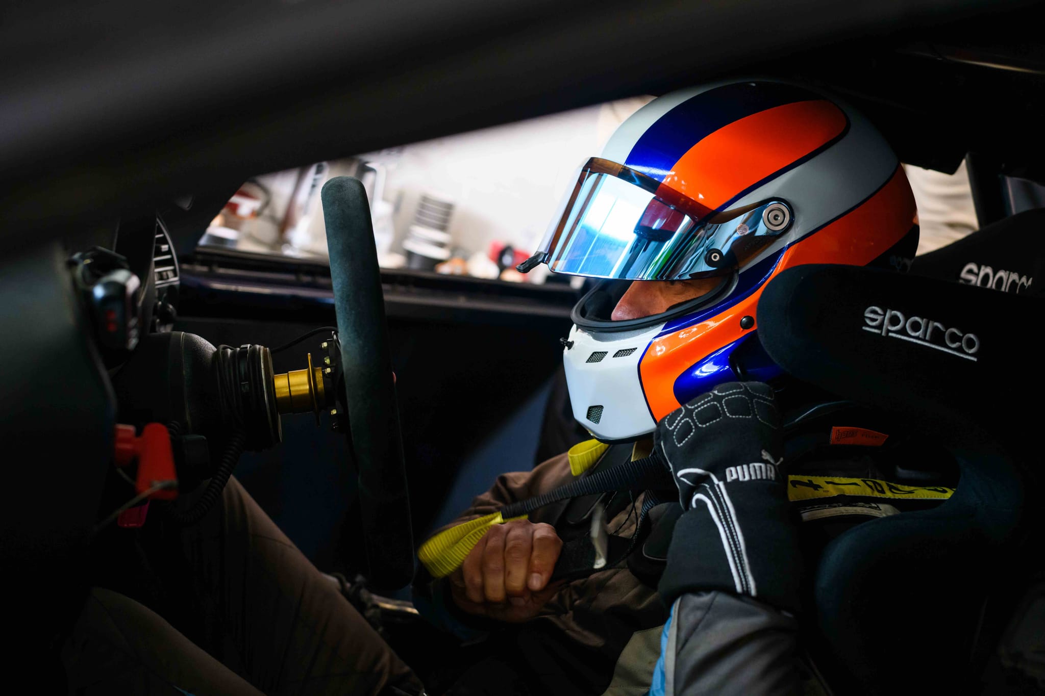 Driver in orange, blue and white helmet seated in the Project E36 cockpit